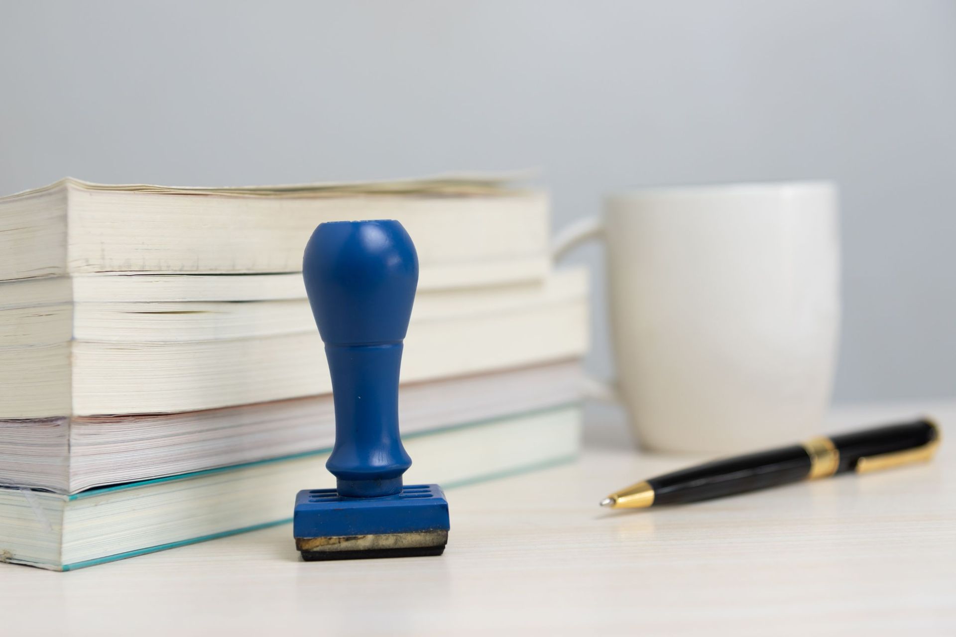 Un sello azul está sobre una mesa al lado de una pila de libros y un bolígrafo.